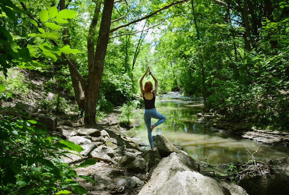 woman in blue tank top and blue leggings standing on gray rock near river during daytime