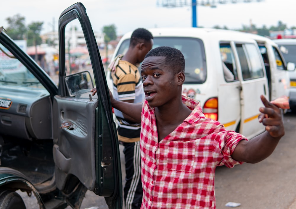 man in red and white plaid button up shirt standing beside black car during daytime