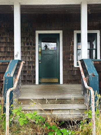 A cozy porch featuring a rustic farmhouse welcome sign hanging near a wooden door with a textured outdoor doormat below.