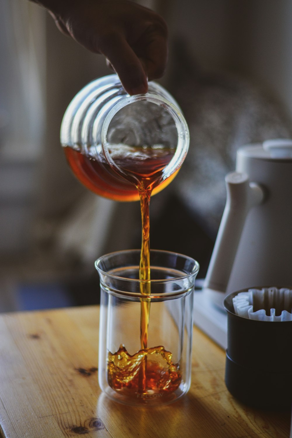 clear glass pitcher pouring brown liquid on clear drinking glass