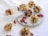 Profiteroles drizzled with chocolate are arranged on a marble platter, surrounded by red currants and purple flowers. Some profiteroles are placed on a white lace cloth, adding elegance to the setting.