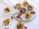 Profiteroles drizzled with chocolate are arranged on a marble platter, surrounded by red currants and purple flowers. Some profiteroles are placed on a white lace cloth, adding elegance to the setting.