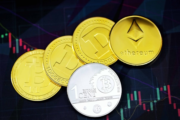 A collection of four coin-like representations of cryptocurrencies including Ethereum, Bitcoin, and Dogecoin. Each coin displays symbols or text related to its respective cryptocurrency. The background features a financial chart with candlestick patterns, suggesting a trading or investment context.