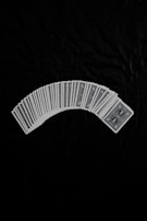 A neatly arranged spread of playing cards with an intricate design on their backs, set against a dark fabric background. The cards form a gentle curve, creating a sense of symmetry and order.