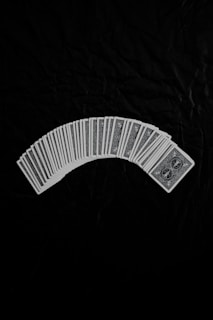 A neatly arranged spread of playing cards with an intricate design on their backs, set against a dark fabric background. The cards form a gentle curve, creating a sense of symmetry and order.