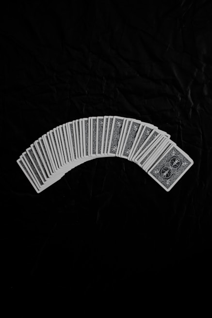 A neatly arranged spread of playing cards with an intricate design on their backs, set against a dark fabric background. The cards form a gentle curve, creating a sense of symmetry and order.