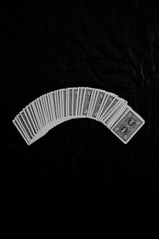 A neatly arranged spread of playing cards with an intricate design on their backs, set against a dark fabric background. The cards form a gentle curve, creating a sense of symmetry and order.