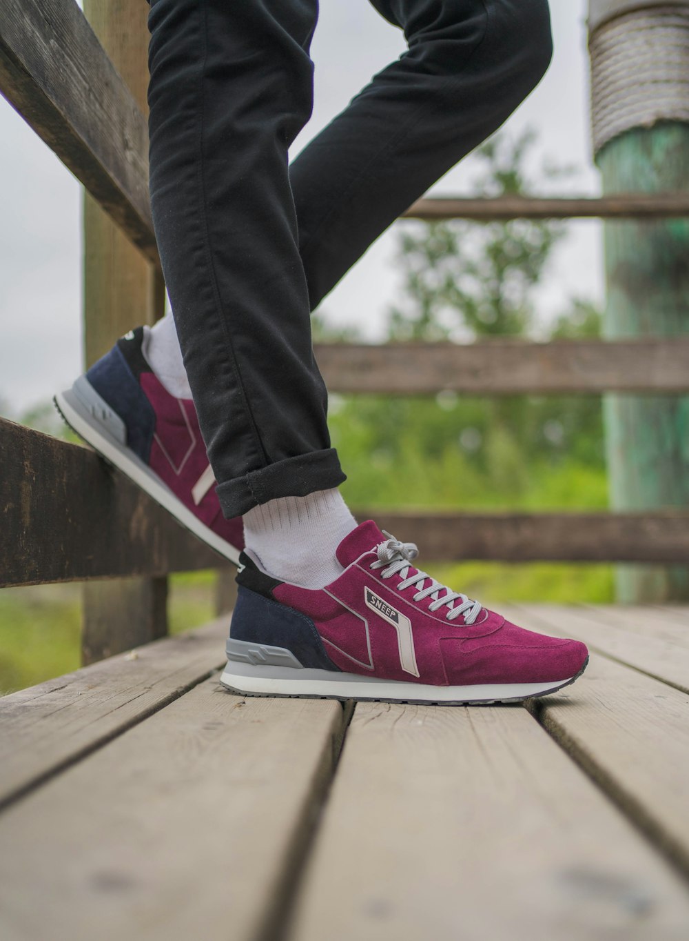 person in black pants and red and white nike sneakers sitting on brown wooden bench