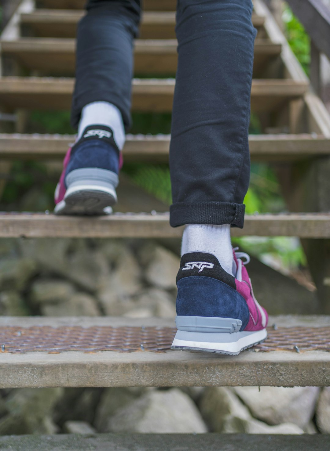 person in blue denim jeans and pink and white sneakers standing on brown wooden stairs