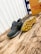 A pair of athletic shoes with a rugged sole is placed on a wooden surface. The shoe on the left is upright, while the one on the right is flipped to display the yellow tread pattern. A cardboard box with the text 'Sneep Crew Made in Spain' is visible in the background.