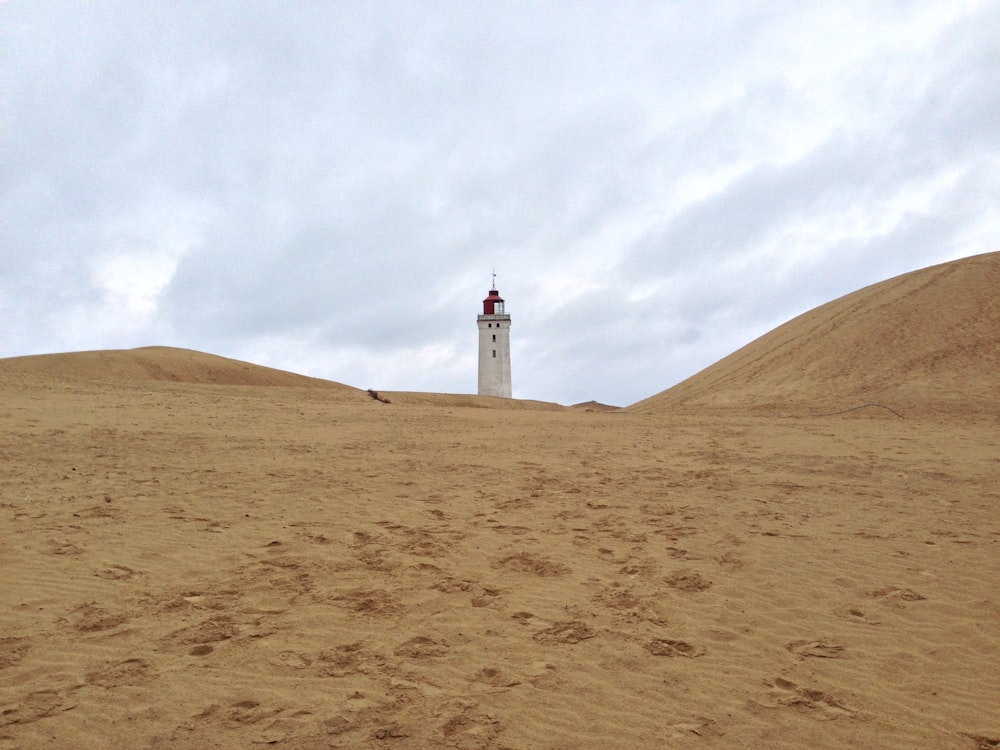 white lighthouse on brown sand under white cloudy sky during daytime