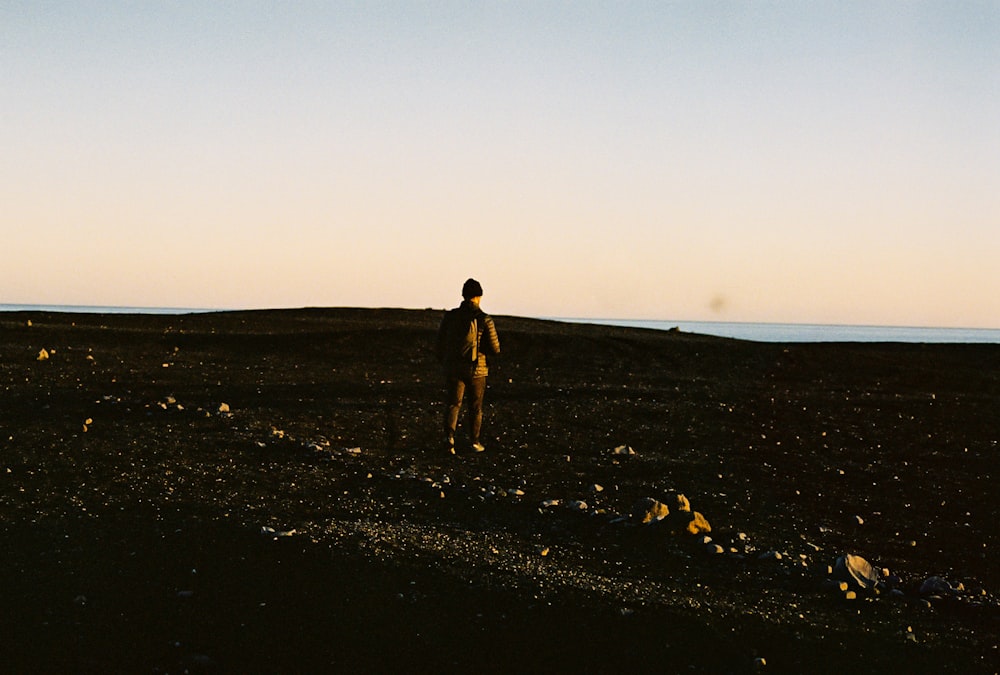 man in black shorts walking on black sand during daytime