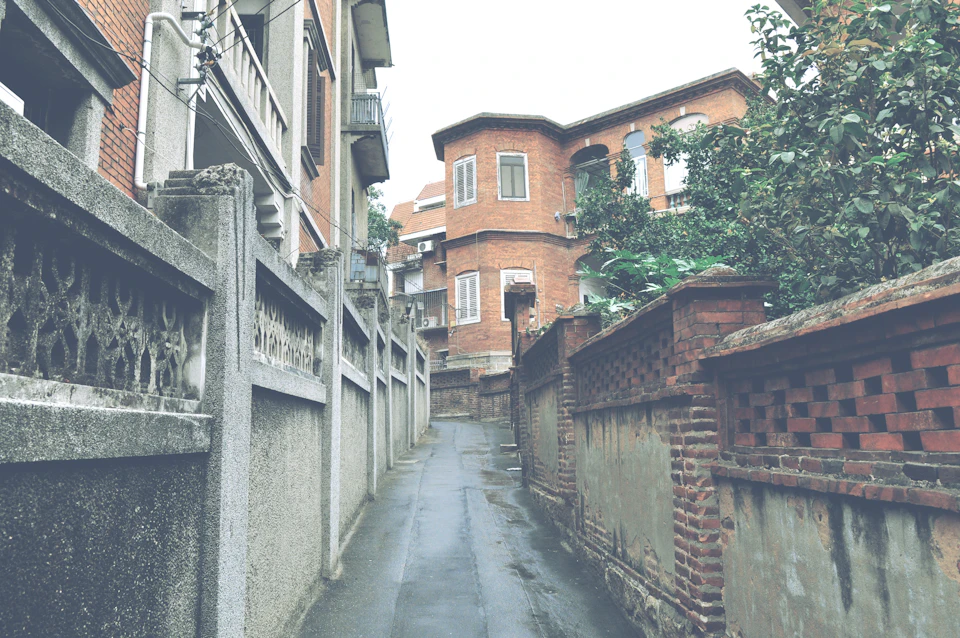 Narrow alleyway between two brick buildings, with trees on either side and surrounding landscape
