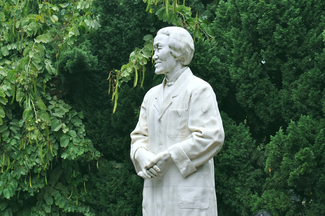 white statue of man near green trees during daytime