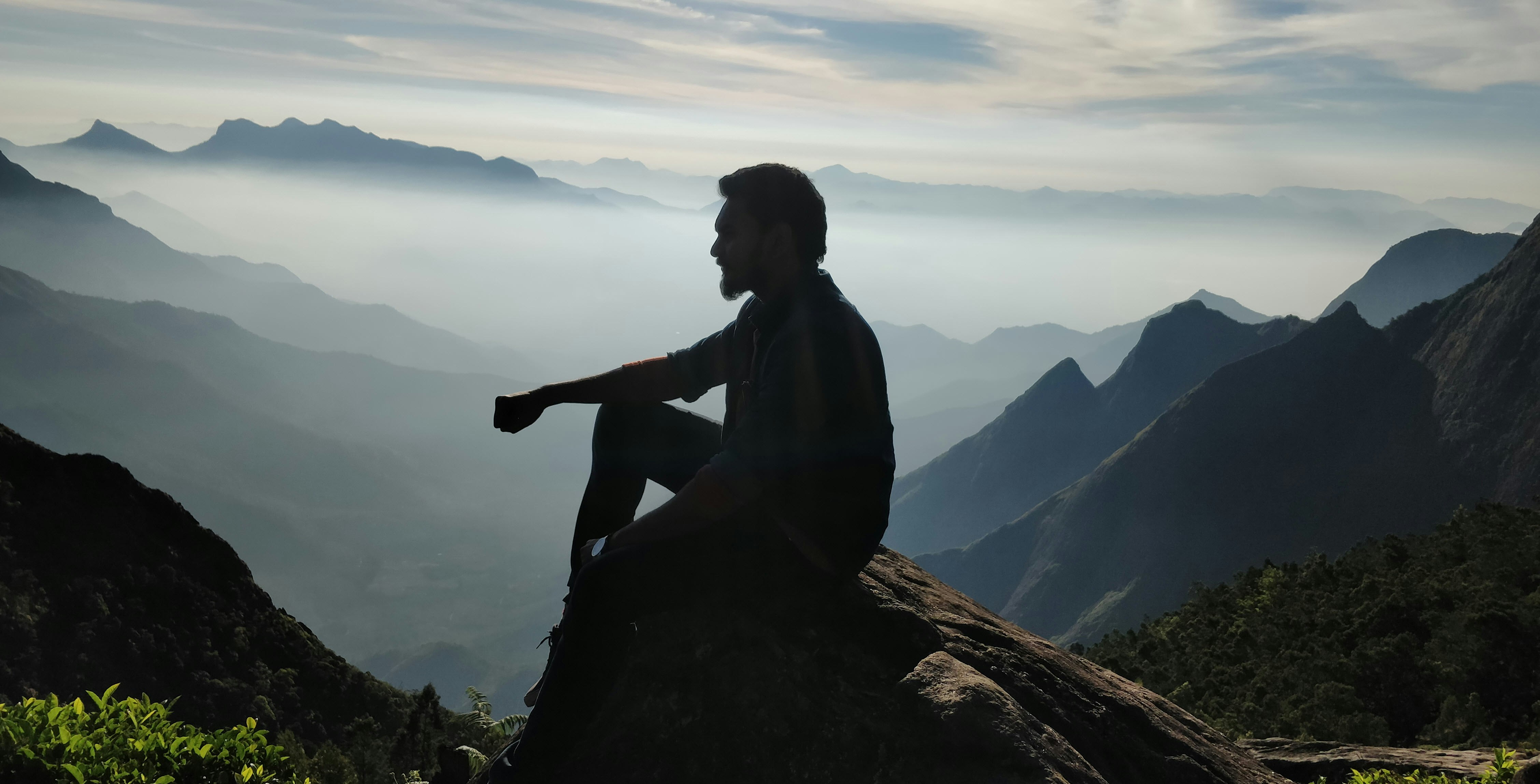 silhouette of man sitting on rock during sunset