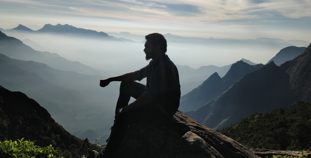 silhouette of man sitting on rock during sunset