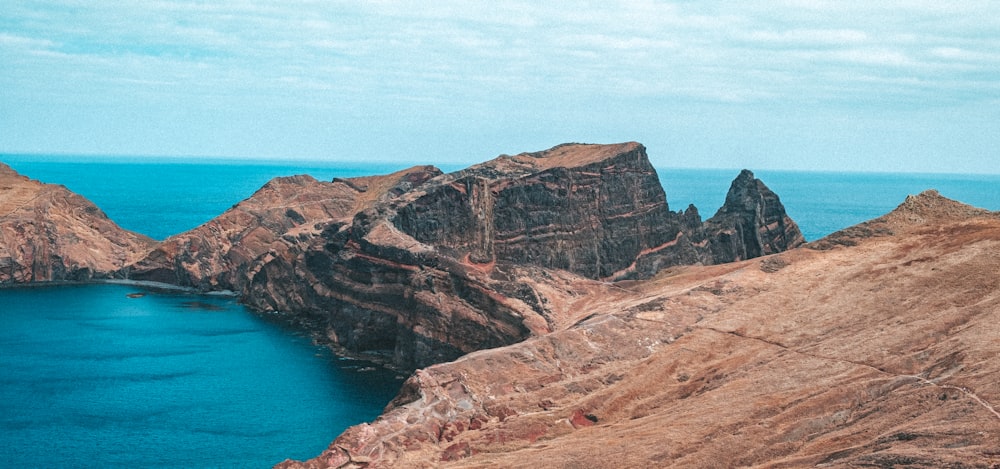 brown rocky mountain beside blue sea under blue sky during daytime