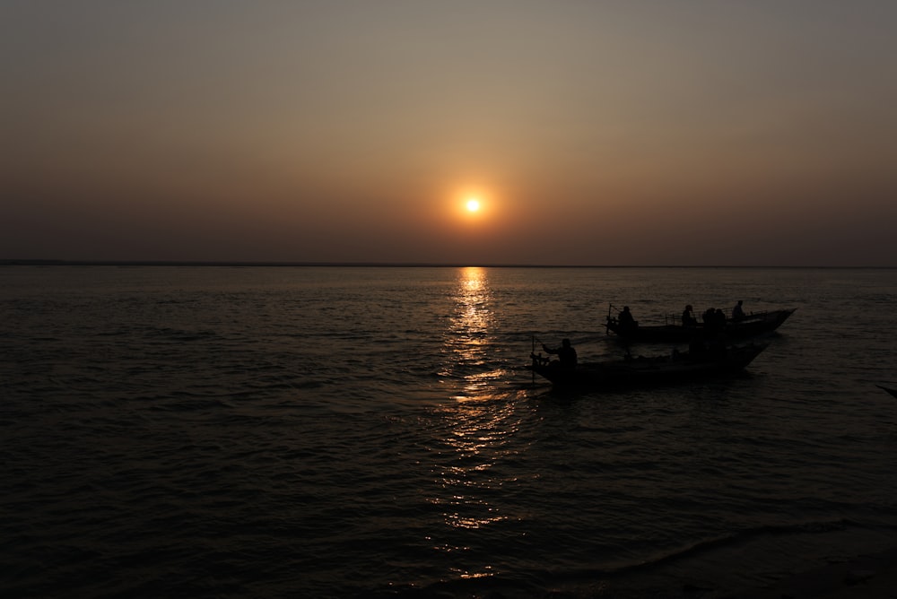 silhouette of people riding boat on sea during sunset