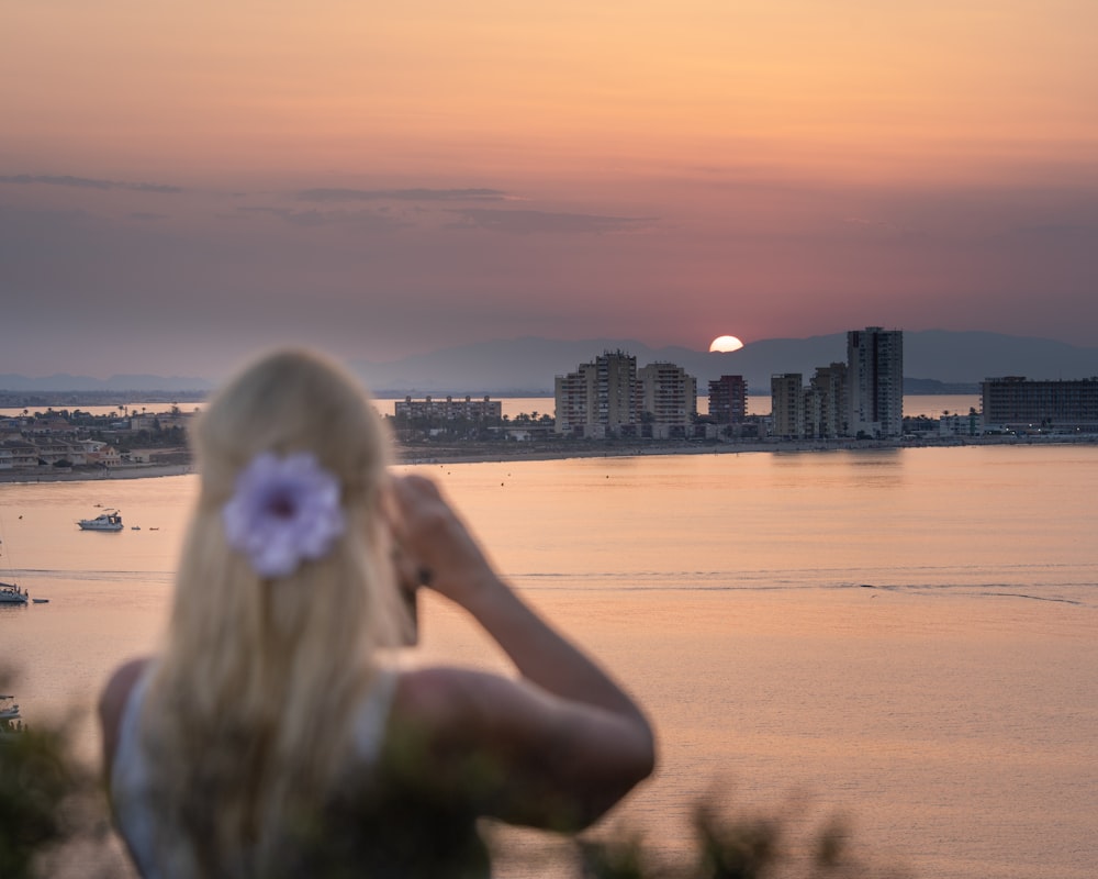 Mujer en vestido blanco de pie en la playa durante la puesta del sol