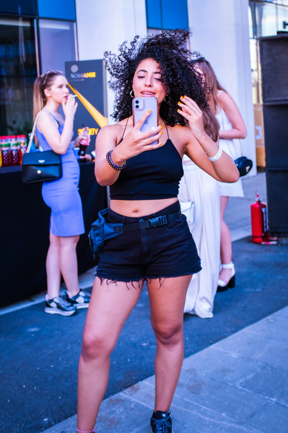 woman in white tank top and blue denim shorts holding white and blue plastic cup