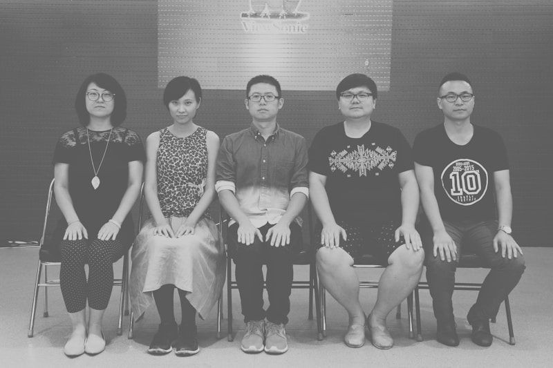 grayscale photo of 4 men and 2 women sitting on chair