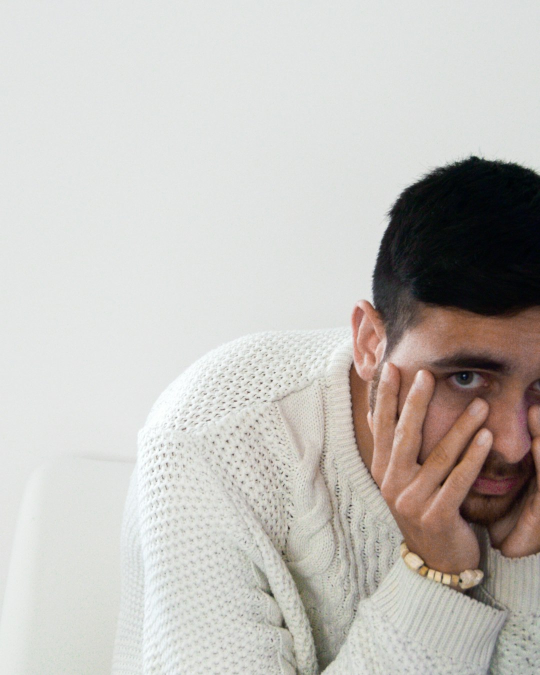 man in white knit sweater covering his face