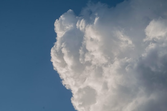 A large, fluffy cloud occupying the right side of the image against a clear blue sky background. The cloud appears dense and bright white, with some subtle shading.
