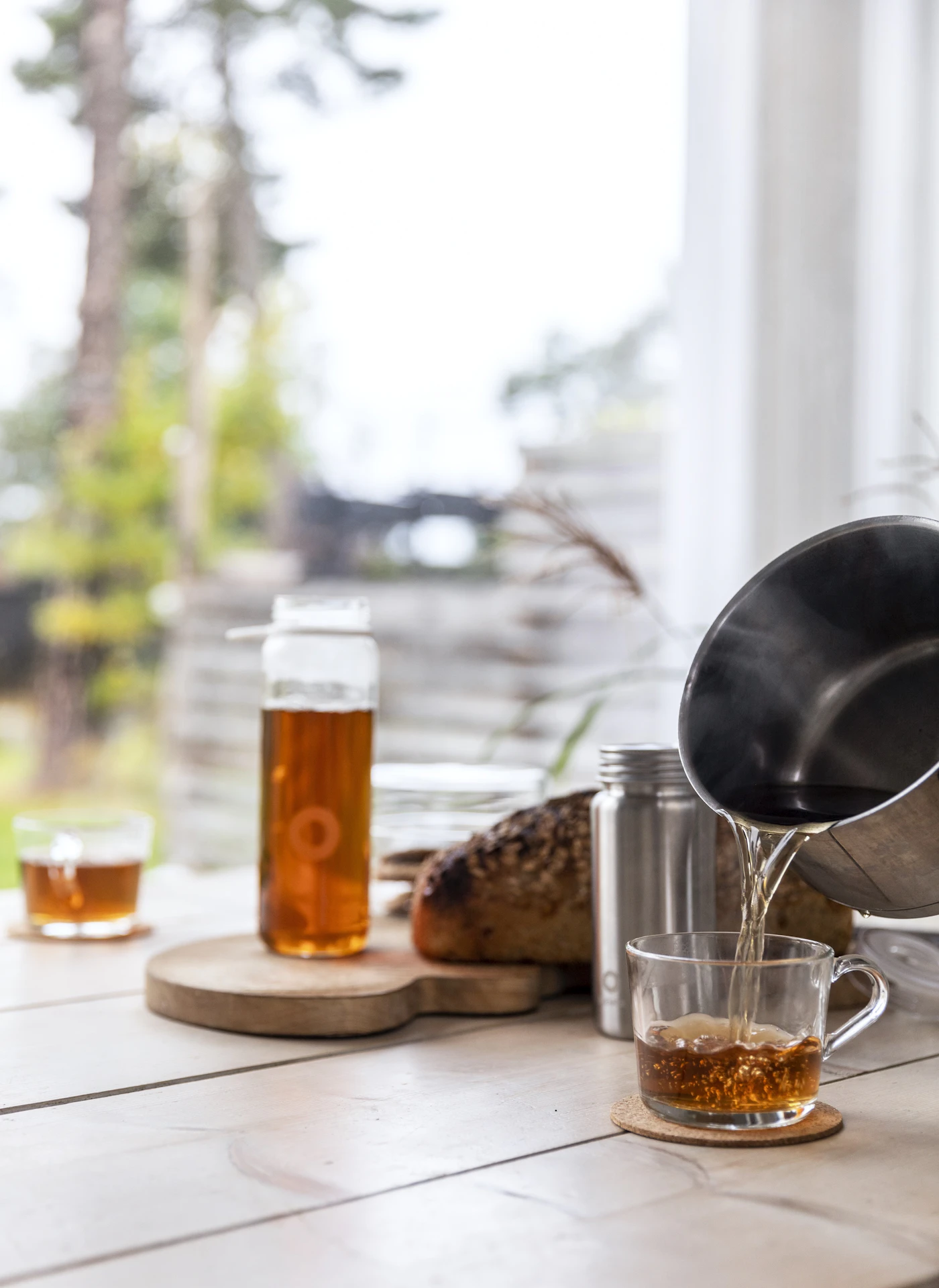 A rustic Nordic table by a window, with a dark loaf of bread and tea being poured
