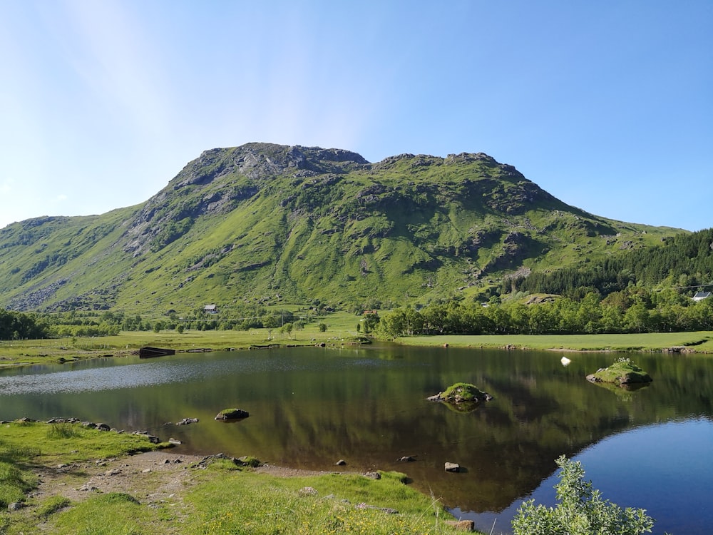 green mountain beside lake under blue sky during daytime