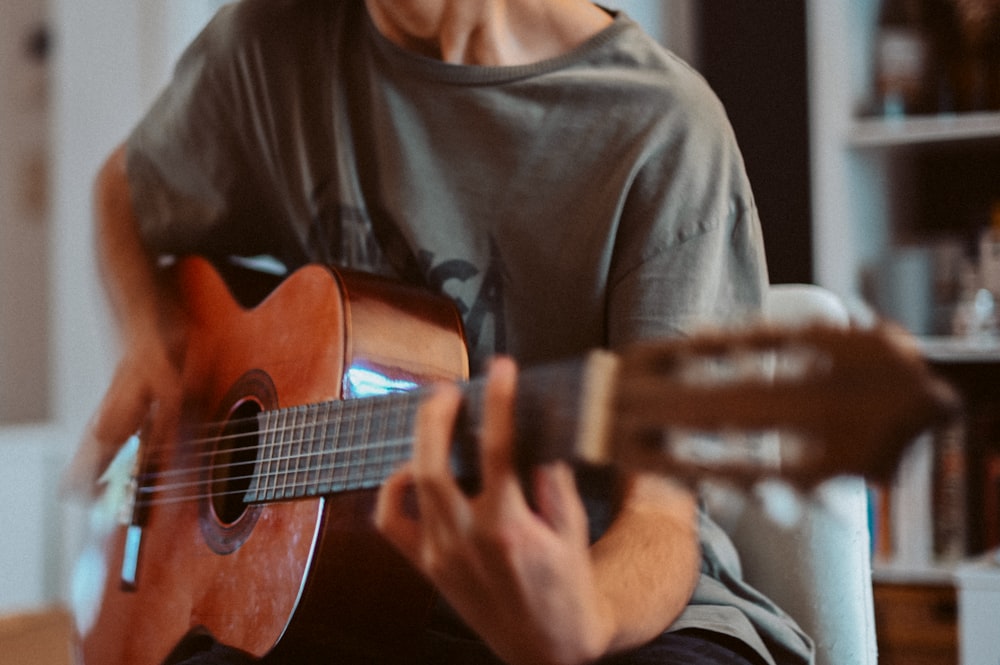 uomo in camicia girocollo grigia che suona la chitarra acustica marrone