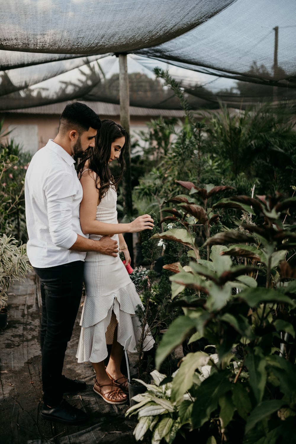 man in white t-shirt and woman in white t-shirt standing near green plants during