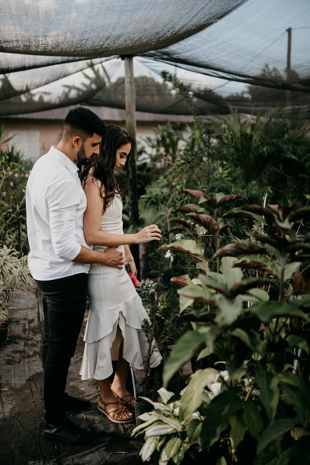 homme en t-shirt blanc et femme en t-shirt blanc debout près des plantes vertes pendant