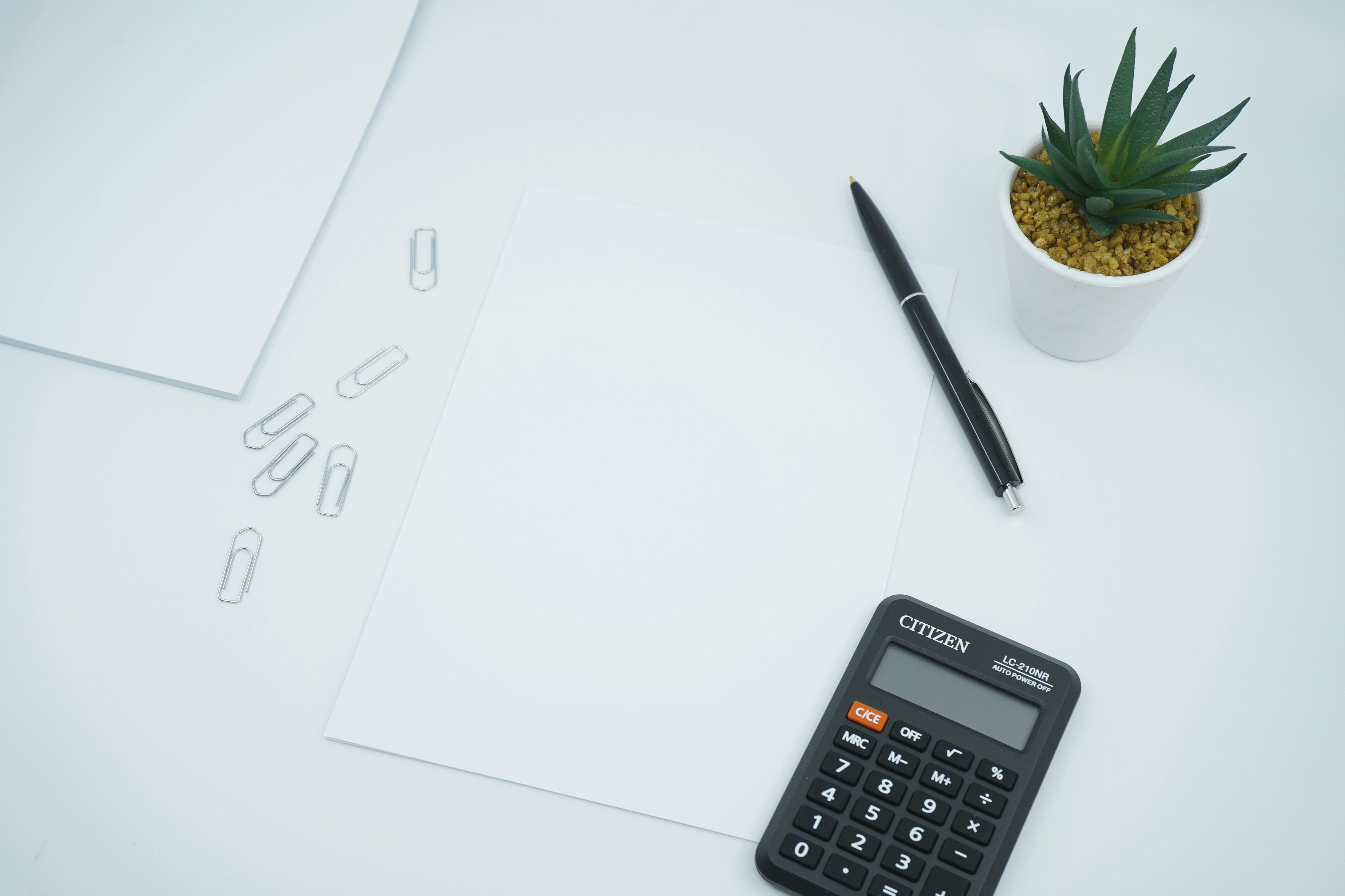 calculadora preta ao lado de uma caneta preta num papel branco de impressora