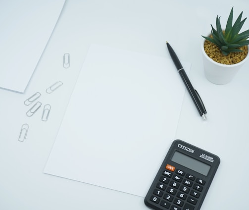 black calculator beside black pen on white printer paper