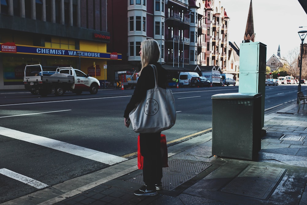 woman in black coat standing on sidewalk during daytime