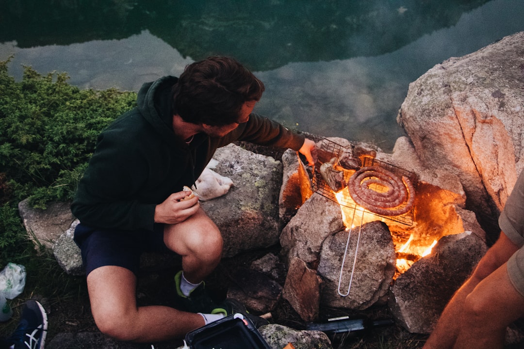 man in black t-shirt sitting on rock near bonfire during daytime