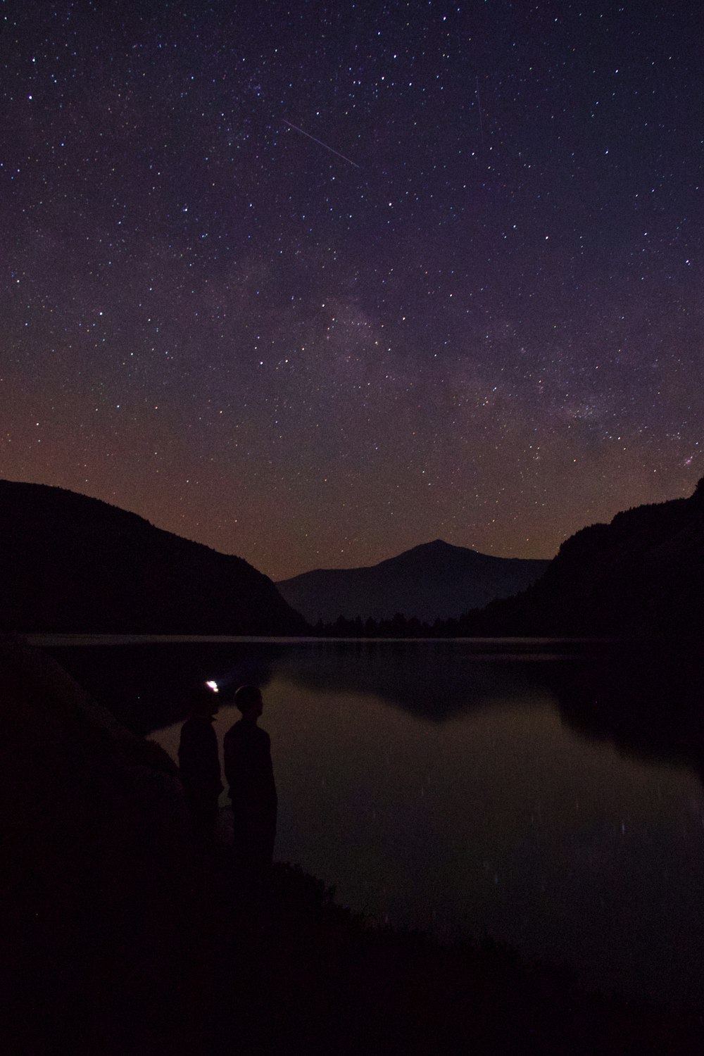 silhouette of 2 person standing near body of water during night time