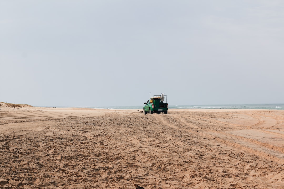 green and black tractor on brown sand near sea during daytime