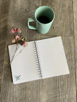 A matte forest green notebook open with handwritten notes and a steaming cup of coffee beside it.