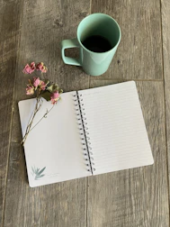 Close-up of a matte forest green notebook with handwritten social media post ideas beside a cup of coffee.