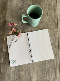 Close-up of a matte forest green notebook with handwritten social media plans beside a cup of coffee on parchment paper.
