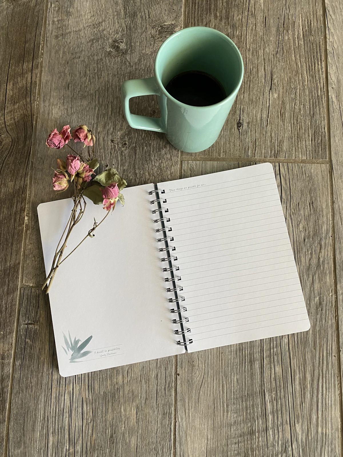 An open notebook beside a ceramic mug of tea on a wooden table