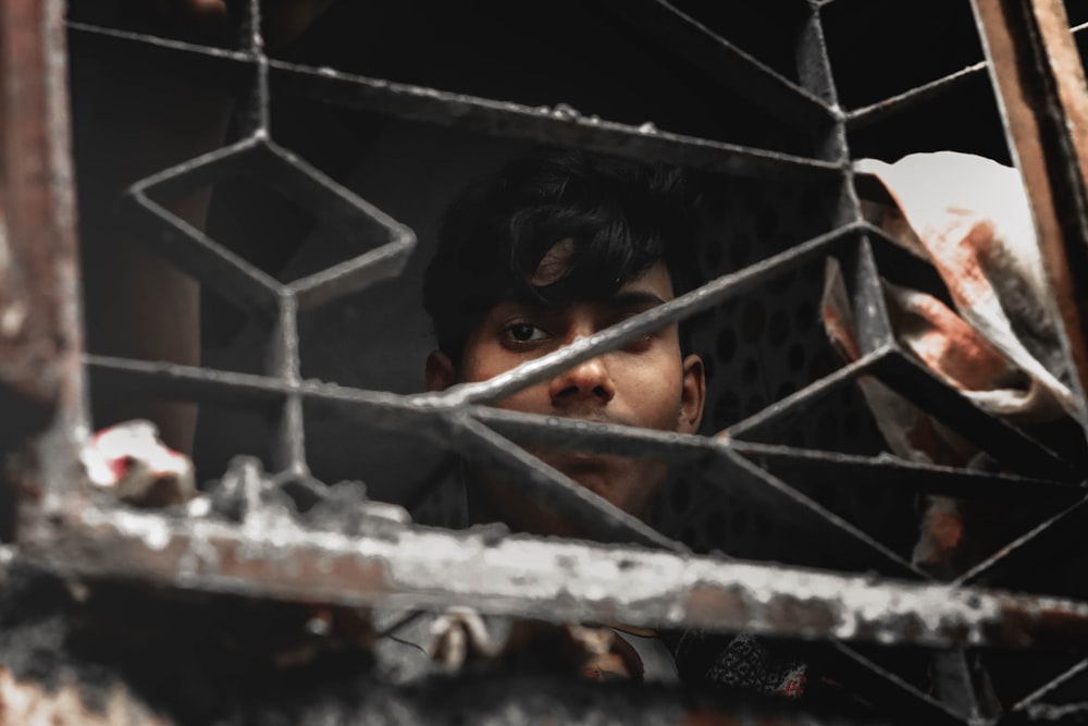 Niño con camisa gris parado detrás de una valla de metal blanco