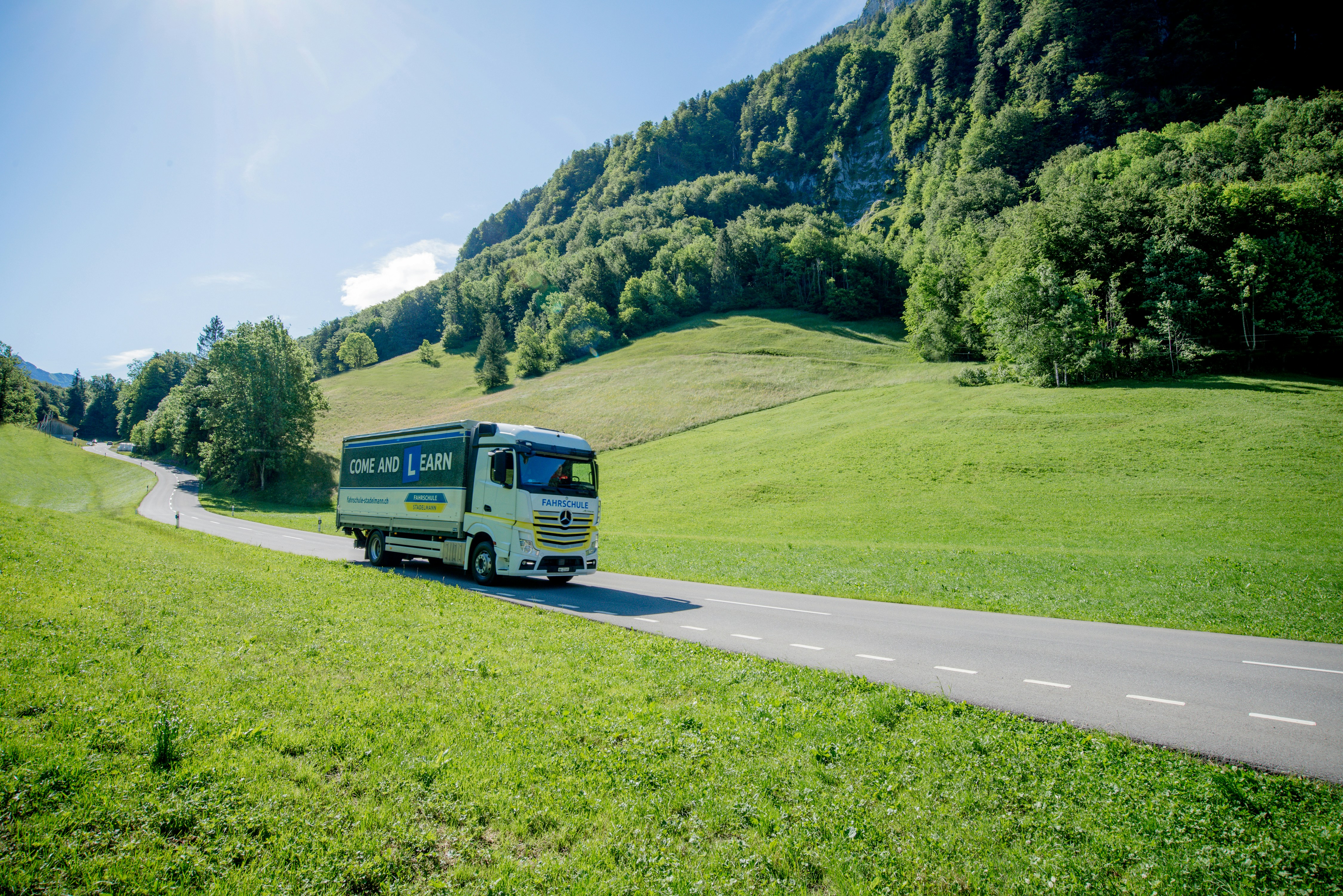 blue van on road near green grass field and green mountains during daytime