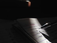 A close-up of hands writing in a diary with warm sunlight casting shadows.