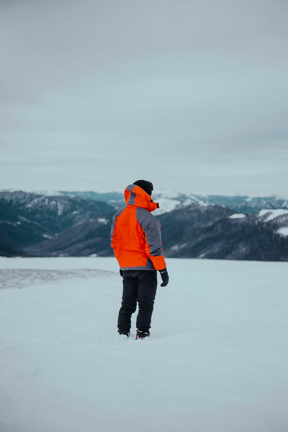 man in orange jacket and black pants standing on snow covered ground during daytime