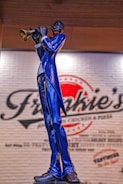 A statue of a musician playing a trumpet, wearing a striking blue suit and standing in front of a wall with a logo that appears to be for a restaurant or café.