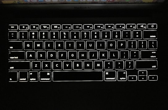 A close-up view of a backlit keyboard on a MacBook Air, with keys clearly visible due to the white illumination against a black background.