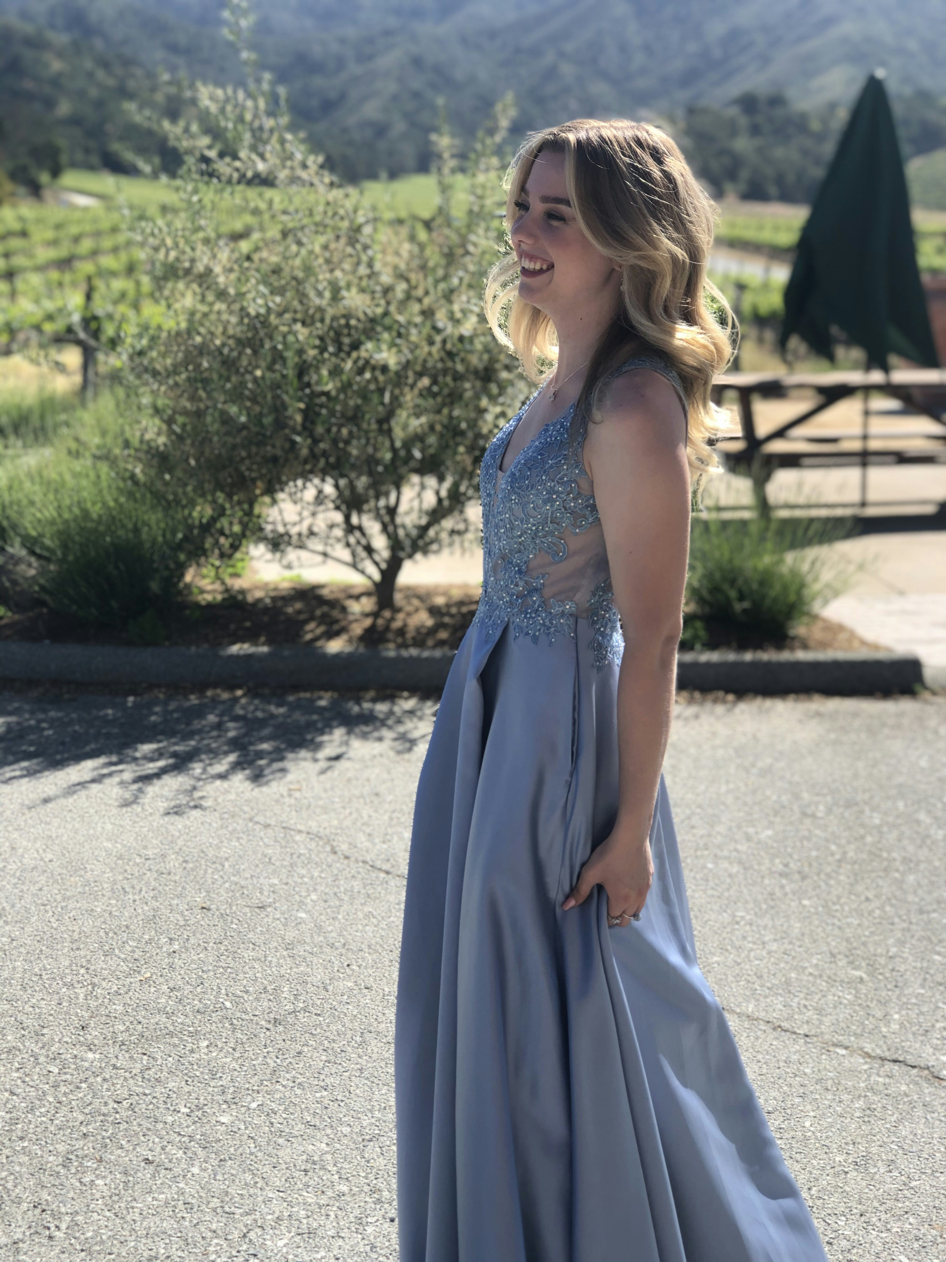 Young woman with blonde hair and bright smile wearing casual summer dress in vineyard setting with warm afternoon sunlight