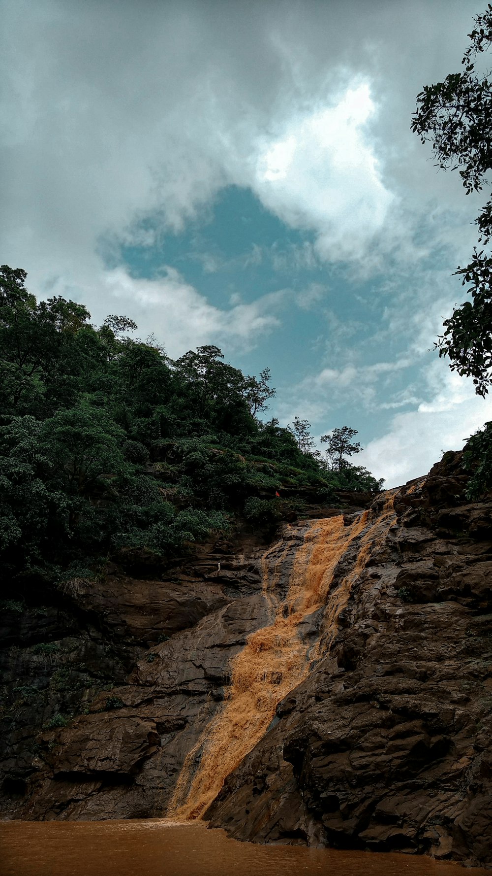 green trees on brown rocky mountain under blue and white cloudy sky during daytime